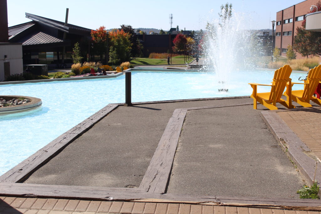 The campus of Cambrian College. It features the fountain, and on the side there are Muskoka chairs.