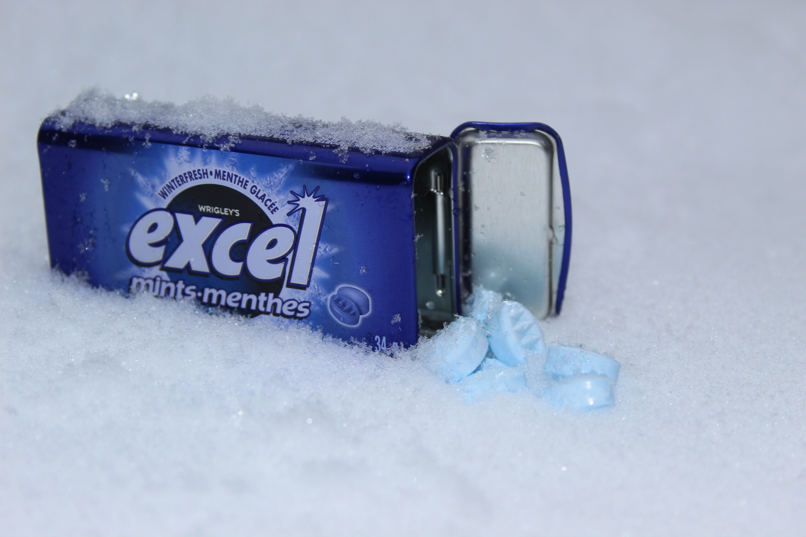 Open excel mints container open in the snow with mints falling out of it.